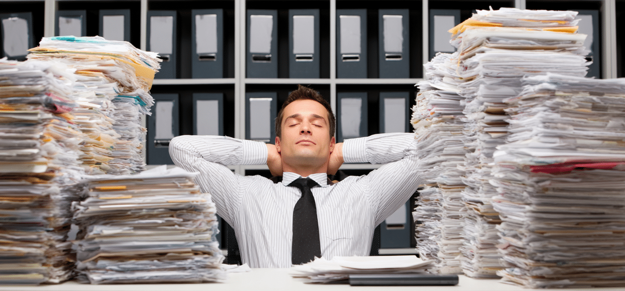 Persona frente a montones de documentos y expedientes, mostrando problemas de organización administrativa